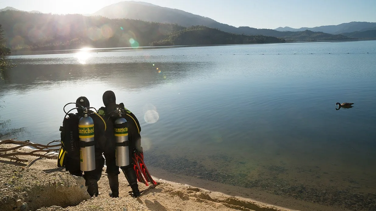 Divers walking along the shoreline with nitrox tanks