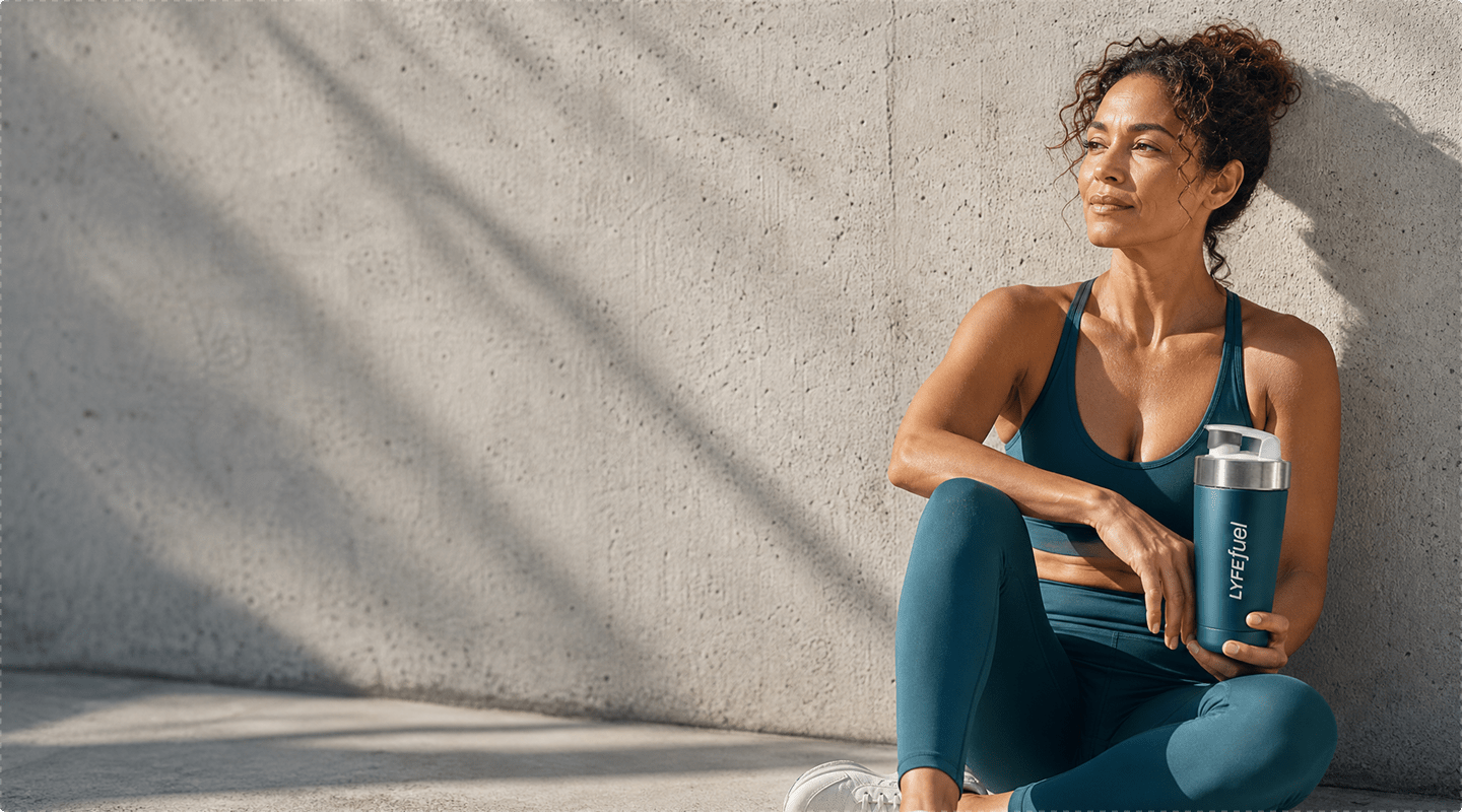 Woman in athletic wear holding a LyfeFuel shaker bottle against a concrete wall