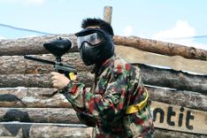 Nastoletni gracz w paintball na tle drewnianej przeszkody