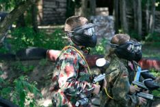 Trójka młodych graczy w paintball w cieniu drzew z okopami w tle