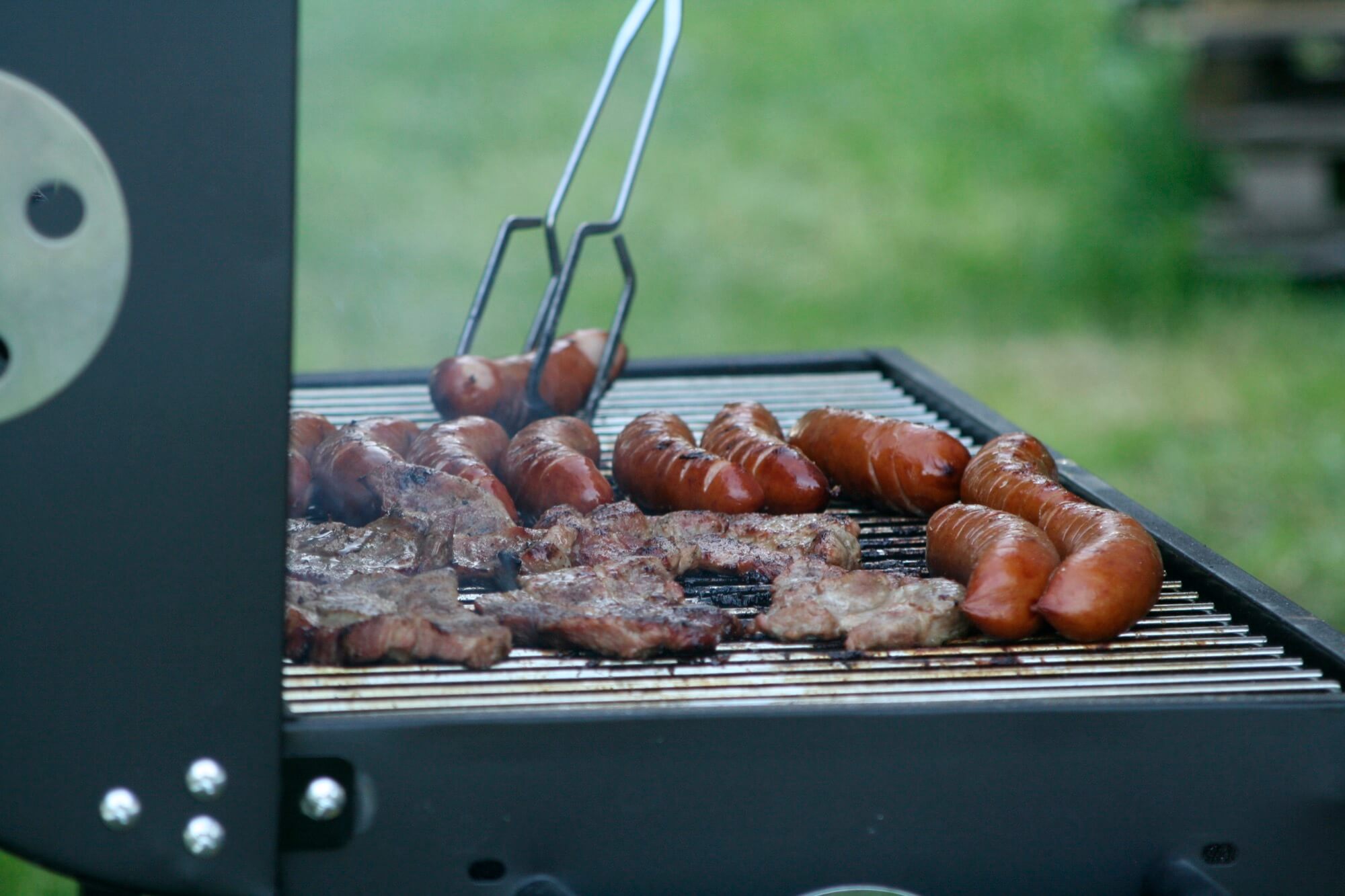 Kiełbaski i karkówka smażące się na grillu