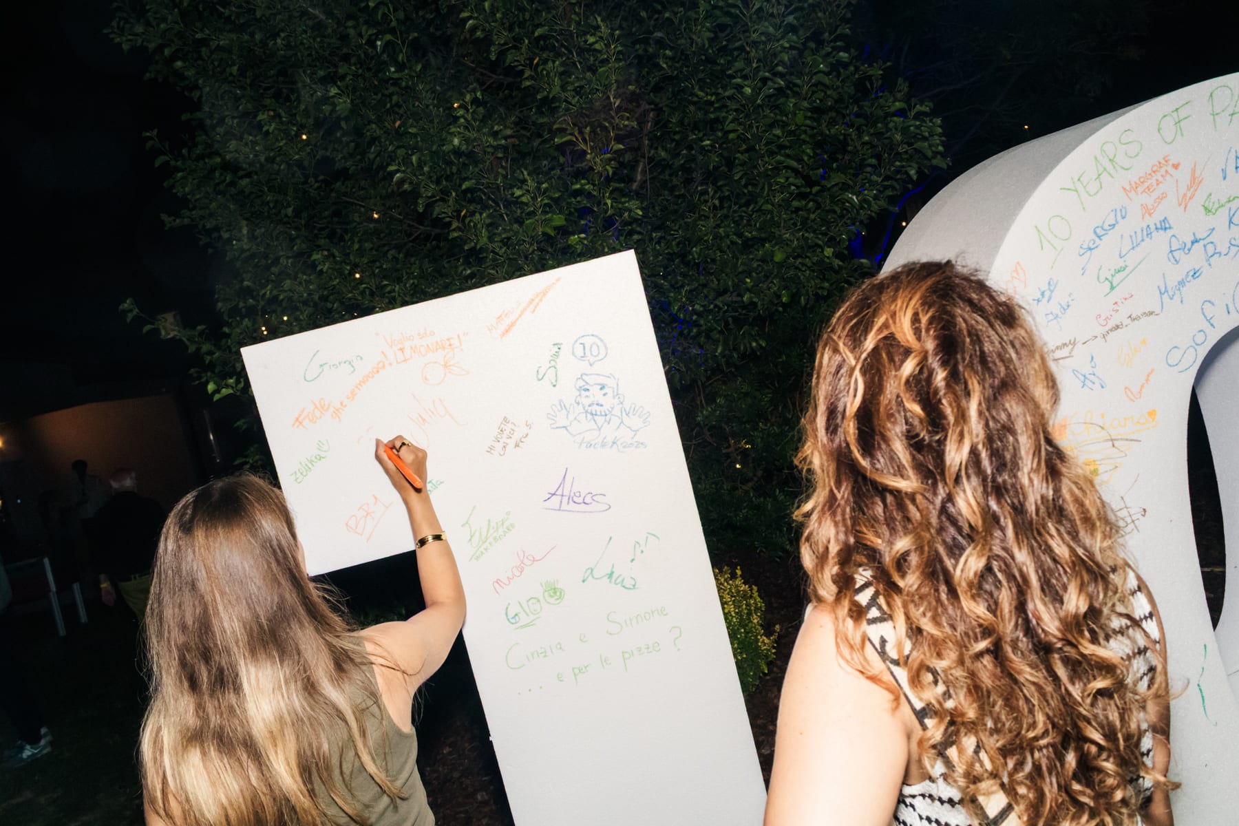 Una fotografia di due ragazze di spalle che lasciano una dedica sul grande 10 realizzato per i 10 years of Palazzina Creativa