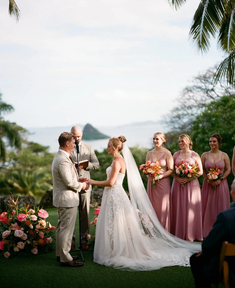 Couple exchanging vows with their bridal party and the ocean behind them in Hawaii