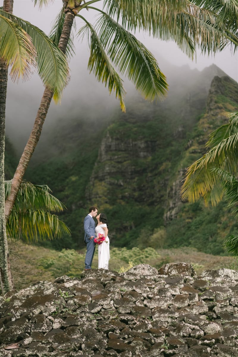 Couple on the lava rocks beneath the misty Ko'olau cliffs at Pālikū Gardens, Kualoa Ranch