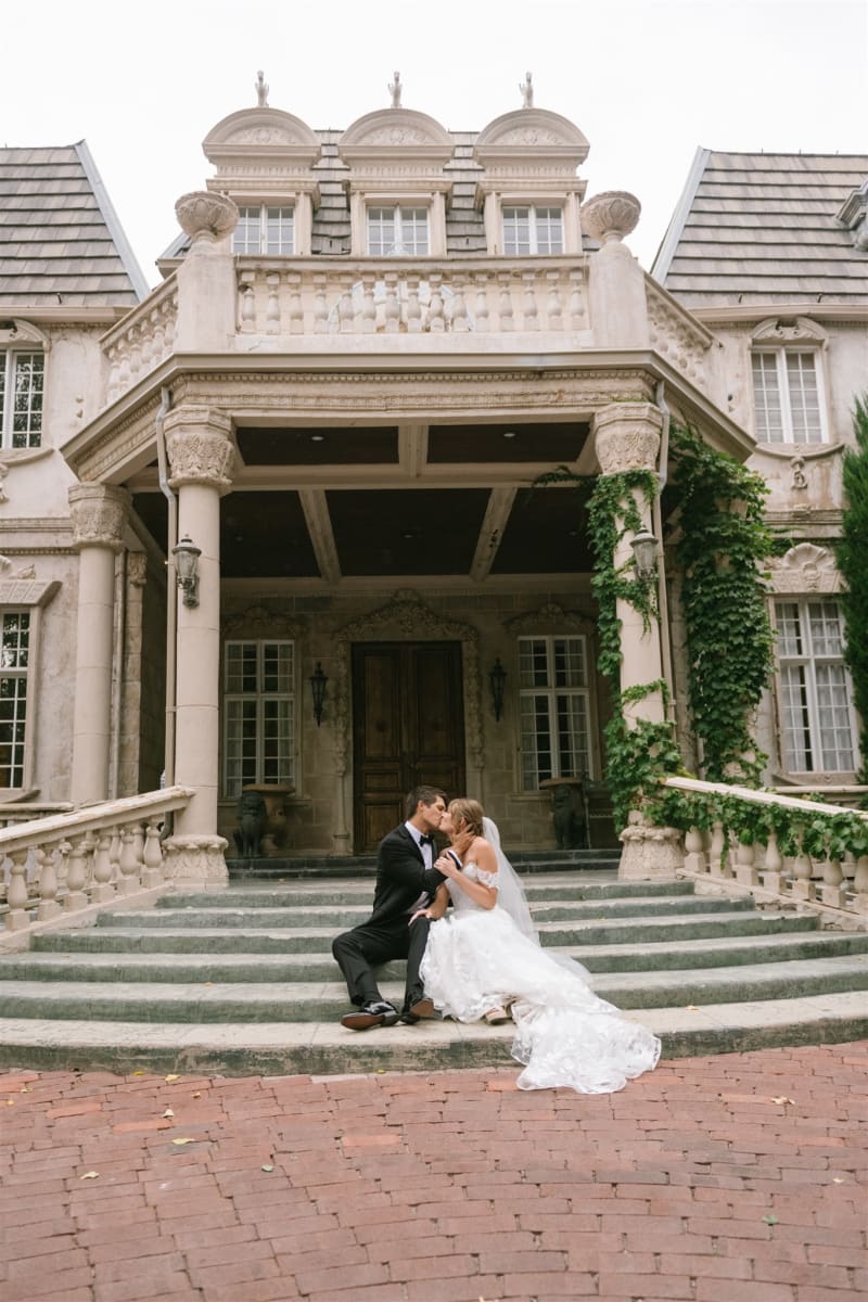 Newlyweds seated on the front steps of the La Caille chateau in Sandy, Utah