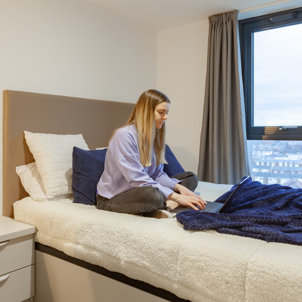 Student on her laptop, sat on the bed using her laptop