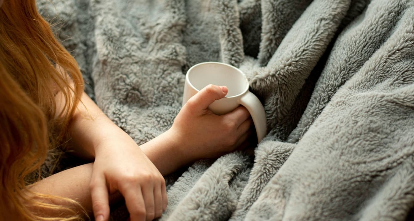 Student snuggled in a blanket with a mug