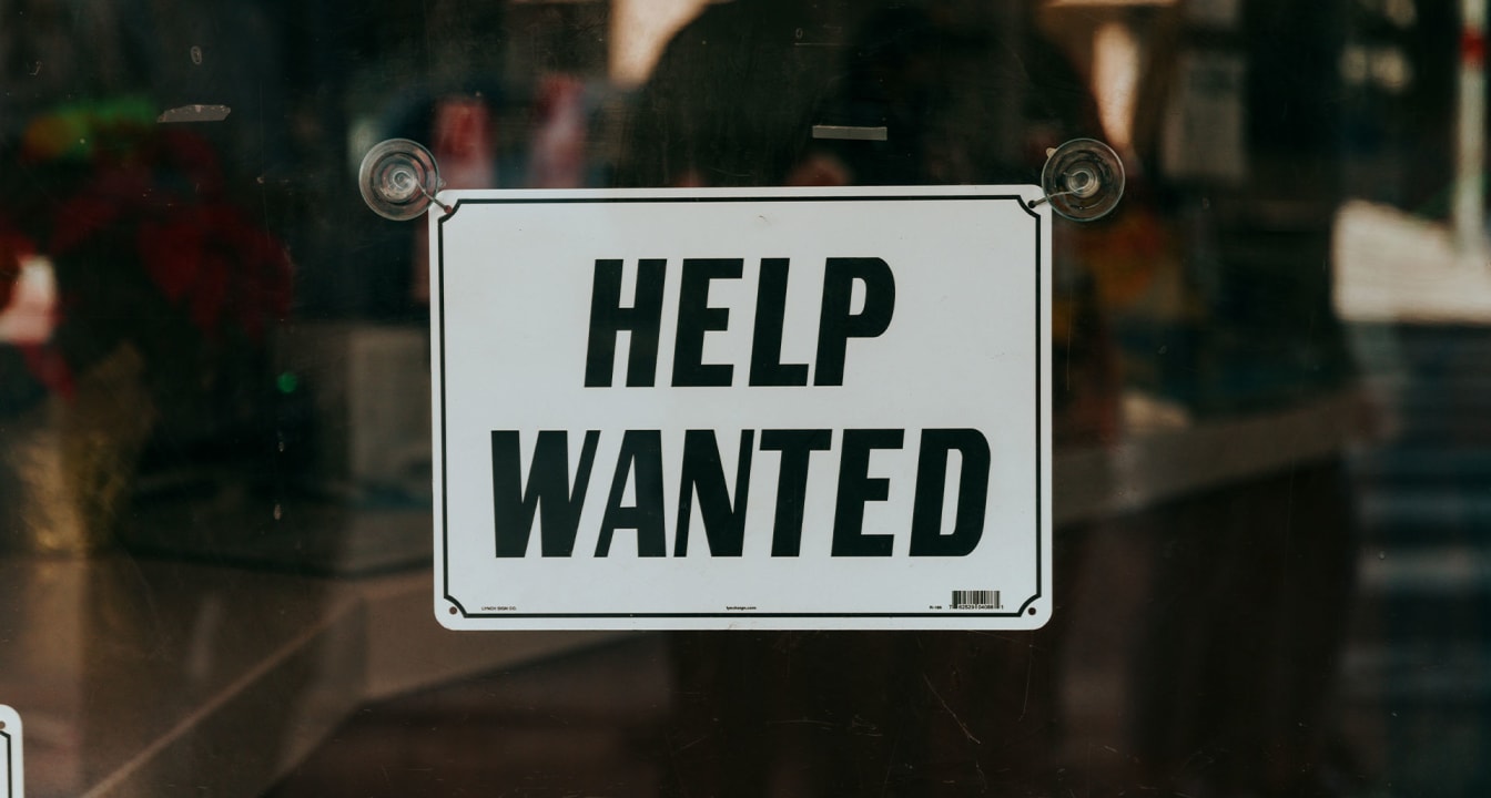 White sign reads 'help wanted' in black text on glass window