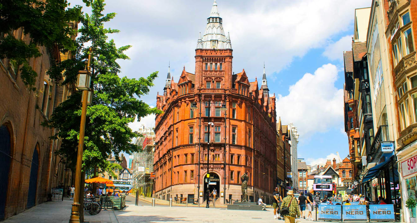 Nottingham town centre street on a sunny day. Tall brown historic building surrounded by shops.
