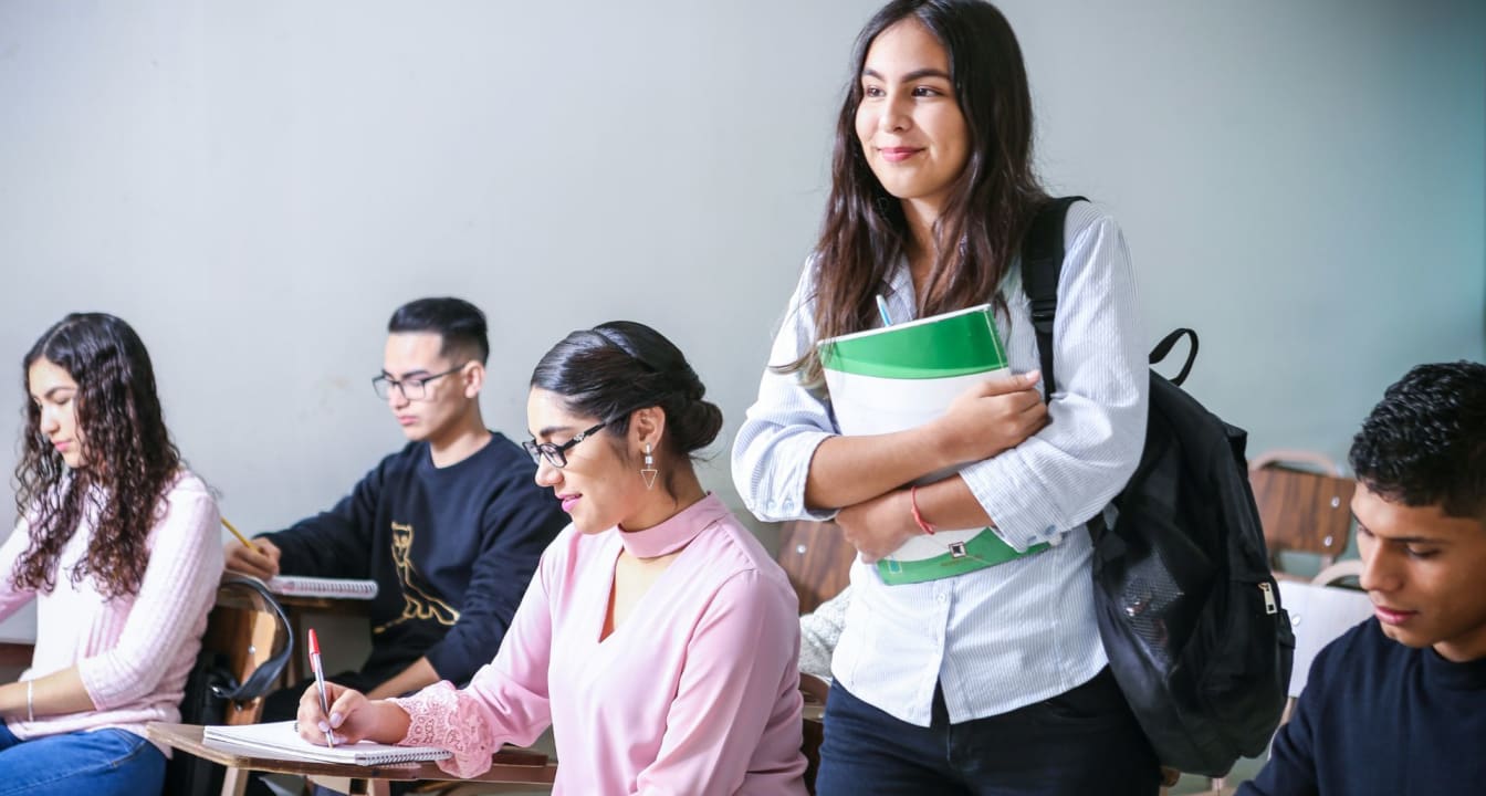 Student stands in class holding green book