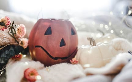 Pumpkin decoration sits on a white blanket surrounded by flowers and fairy lights