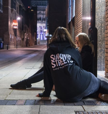 An outreach worker sits on the floor talking to a woman