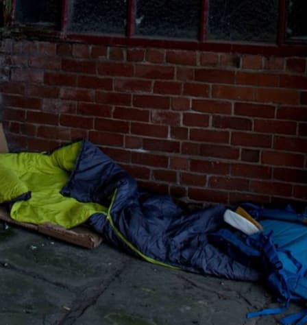 A blue sleeping bag is on the floor, next to a brick wall. A flattened carboard box is underneath.
