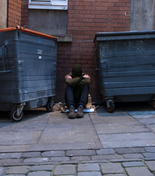 A person is sat on the floor between two bins.