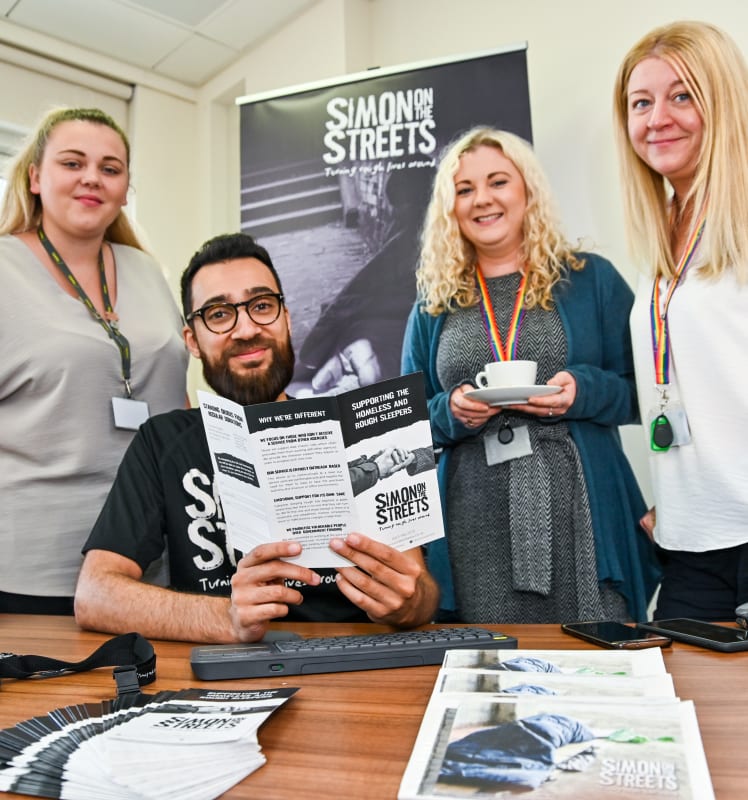 4 people at a table, looking at Simon on the Streets leaflet