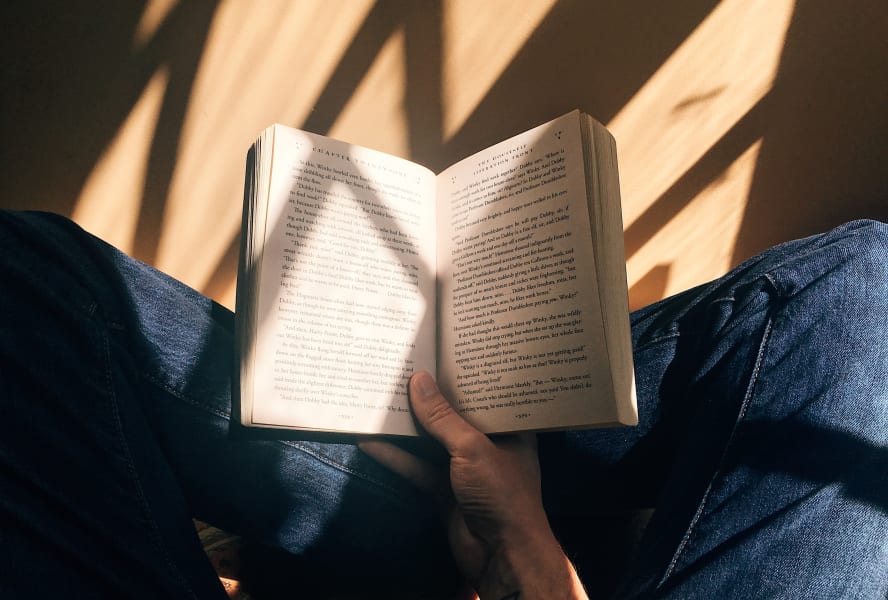 Open book held by male hand over blue jeans