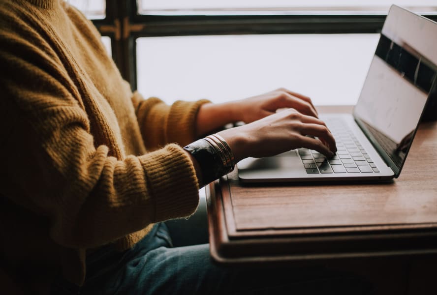 Student wearing a yellow jumper types on a laptop