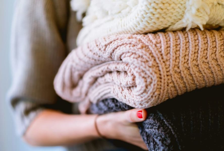Student holds a stack of black, pink, and cream knitted blankets.