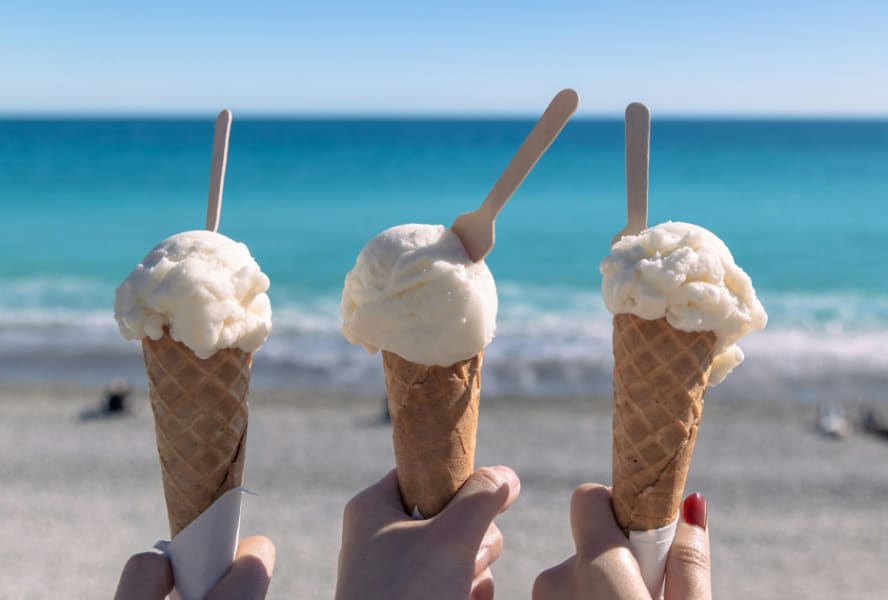 Three ice creams being held at the beach