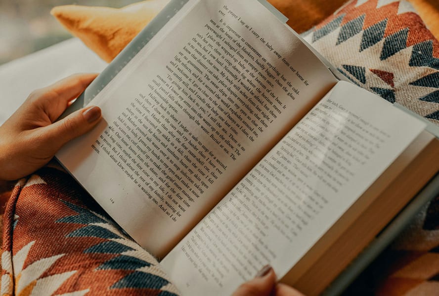 Open book is held open, balanced on an aztec printed cushion