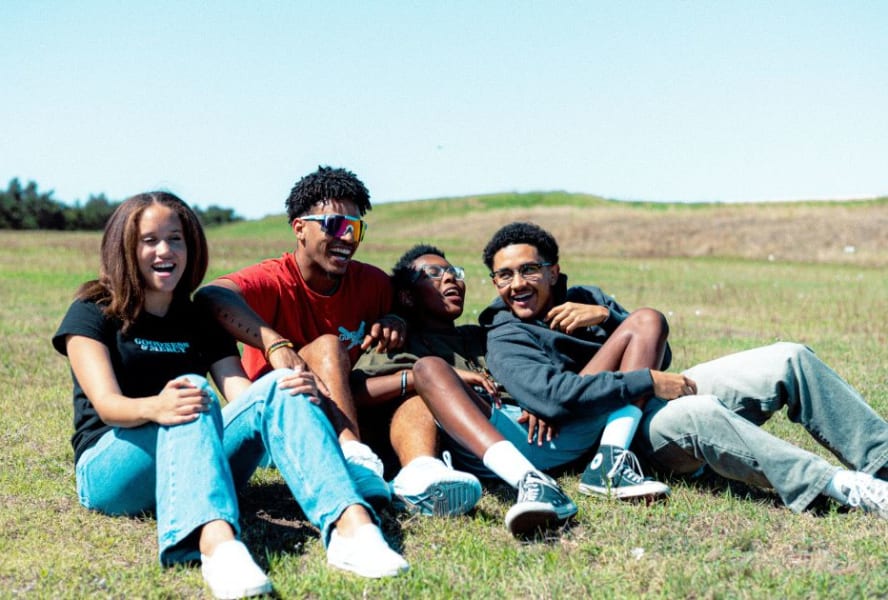 Four students sit laughing in a field