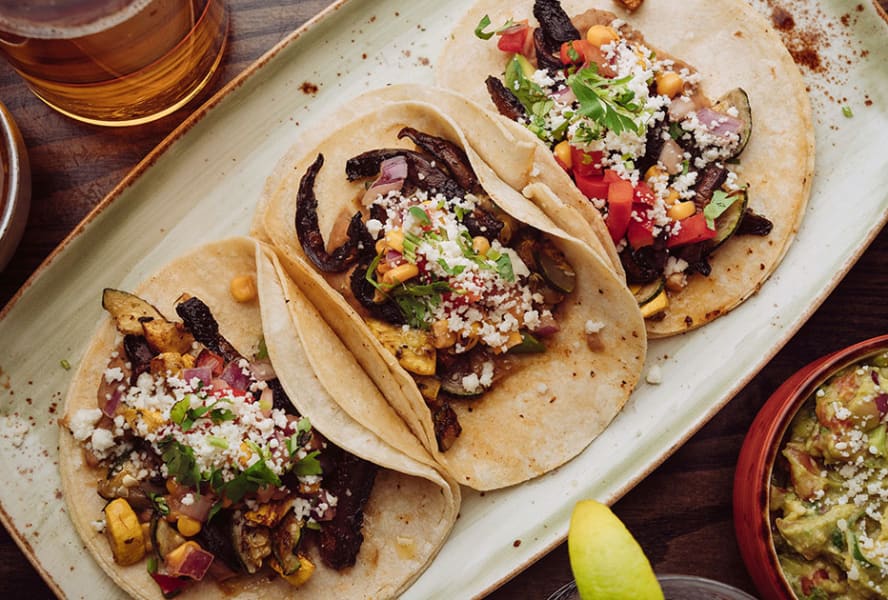 Three tacos with cheese, dips and vegetables