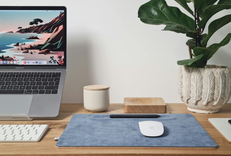 Laptop, mouse mat, candle and plant on a wooden desk