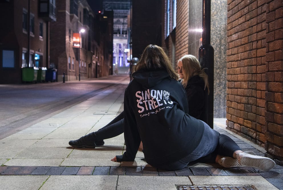 An outreach worker sits on the floor talking to a woman