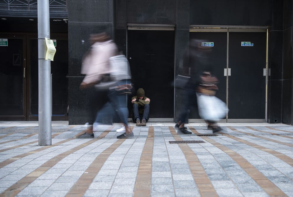 A homeless man sits in a doorway as people walk past