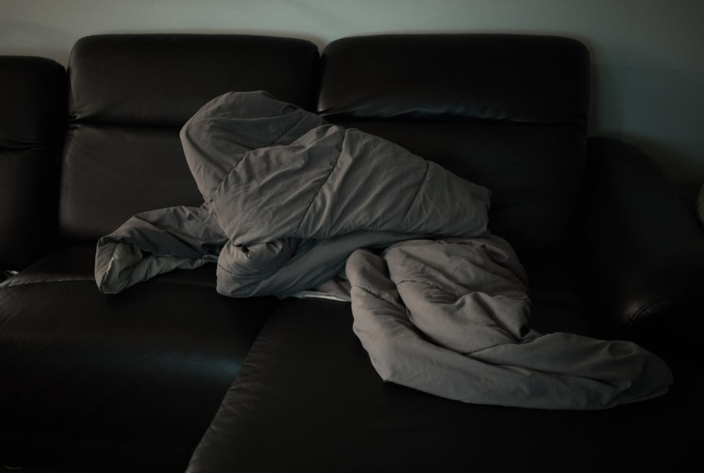 A close up of a black leather sofa with a grey duvet bunched up on it