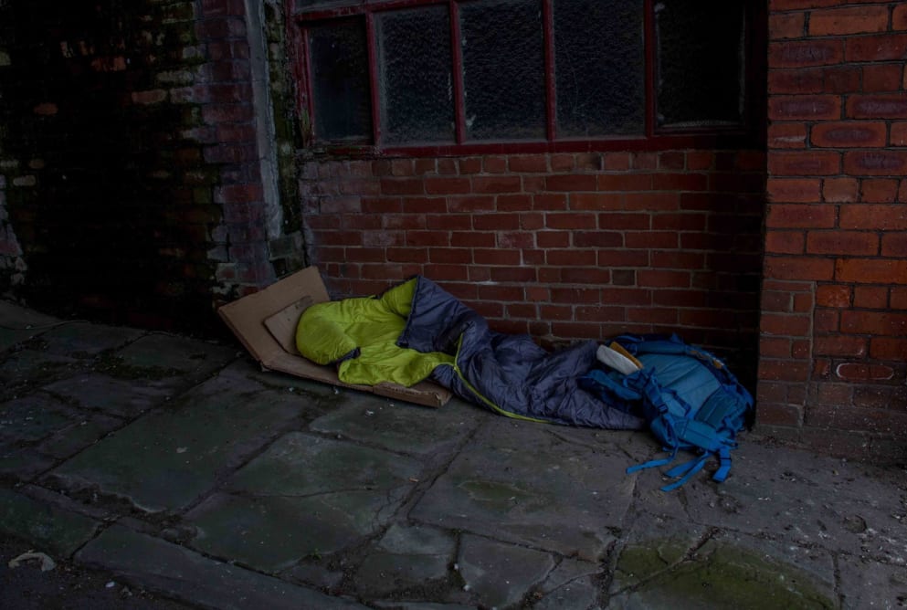 A blue sleeping back and rucksack are on the floor underneath a window