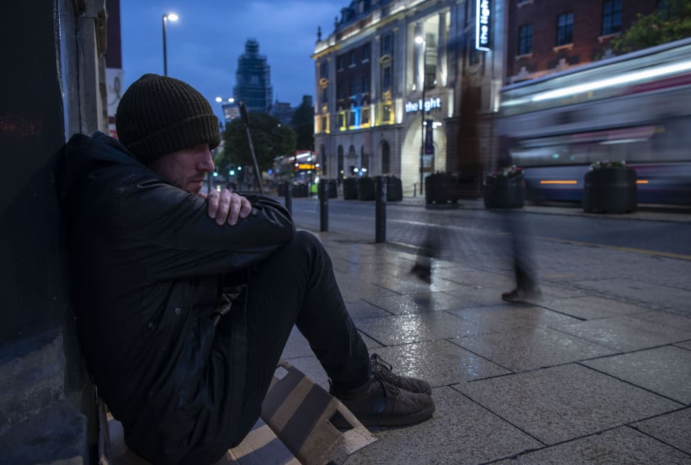 A person sits on the side of a street - Simon on the Streets