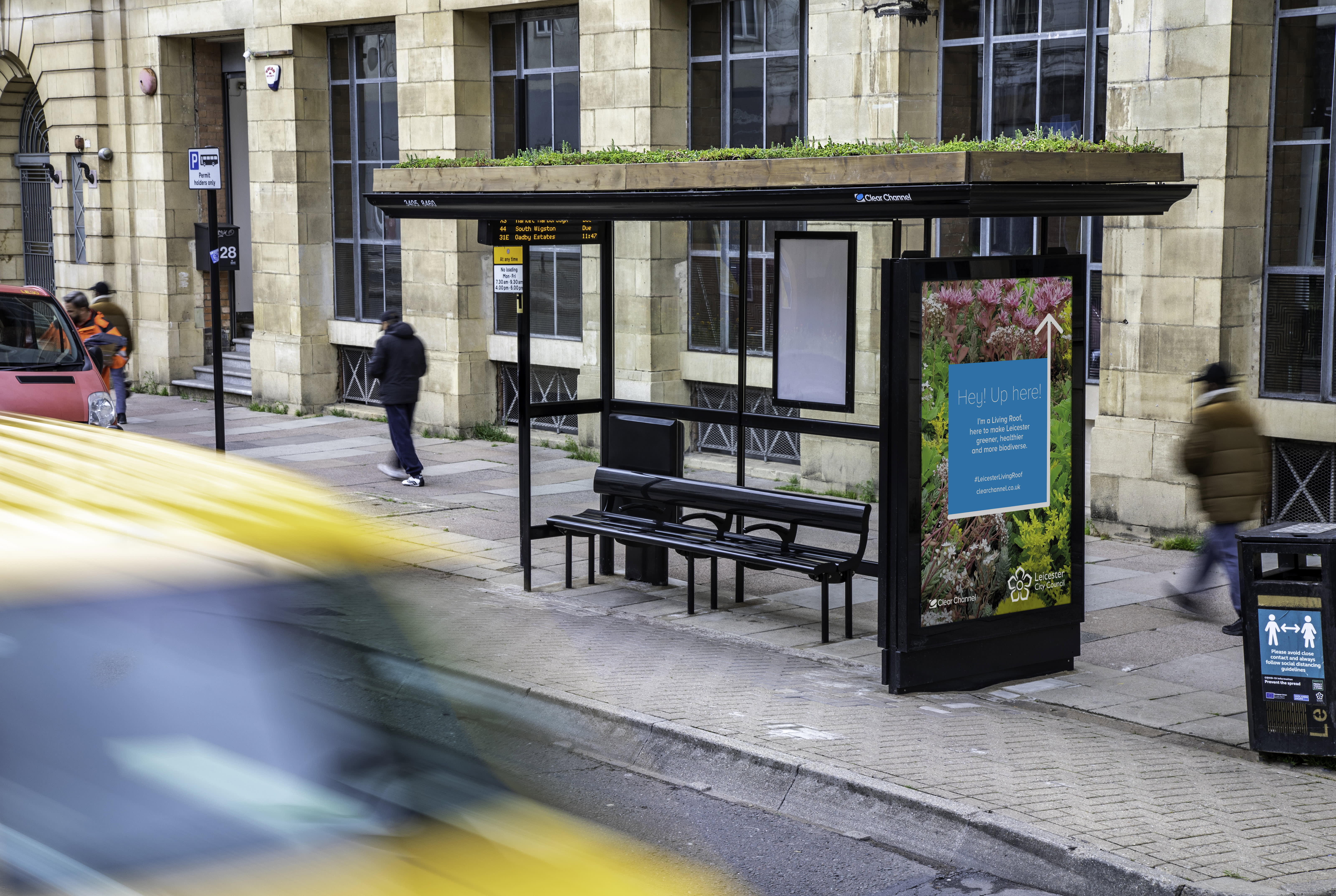 A living roof bus shelter in Leicester with people walking past.