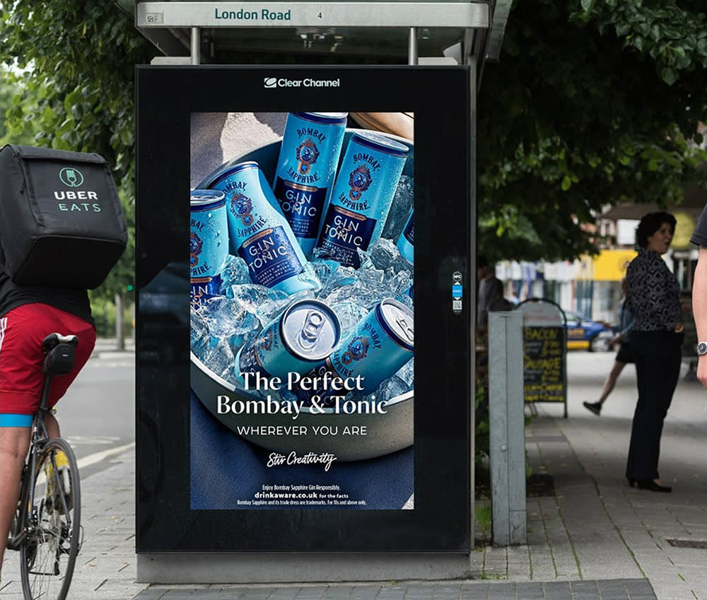 Gin and tonic pre-mixed drink advert on a digital bus shelter in summer with a cyclist passing by