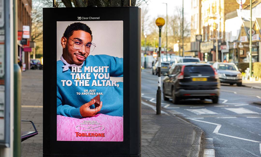 Chocolate bar poster with young black man smiling and words saying 'he might take you to the altar, or just to another bar', on a digital bus shelter unit next to the road