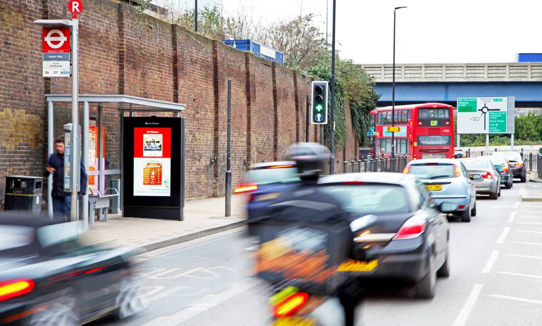 Adshel Live screen on bus stop on a busy road showing Camelot Lottery advert