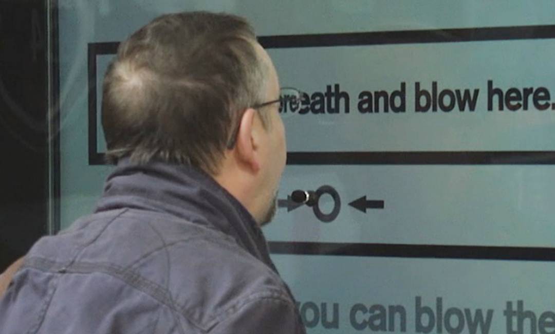 Male blows into a hole in screen as part of Cancer Research creative