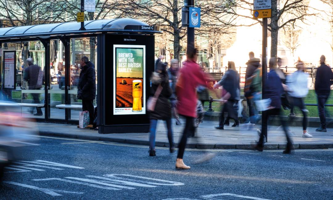 Digital screen on a bus stop of a busy road showing Carling advert.