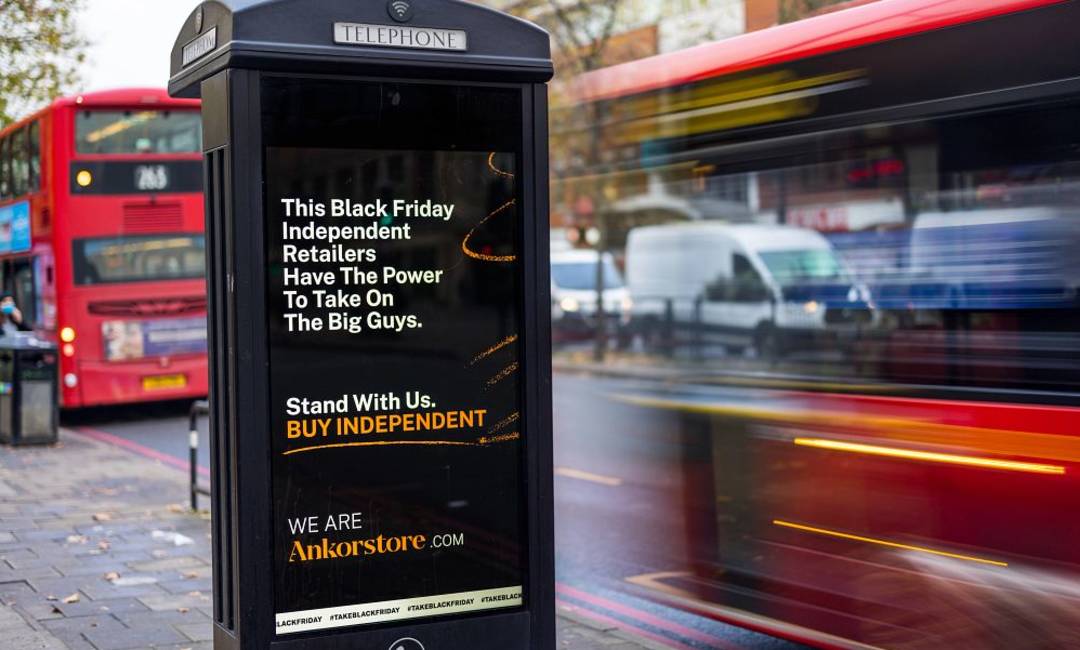 An ad for an independent retail website on Adshel Live screen on a phone kiosk with buses going past