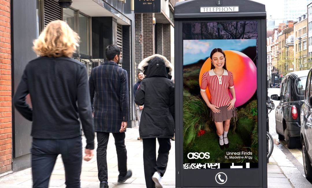 ASOS advertising on the side of a payphone as pedestrians walk by during the middle of the day