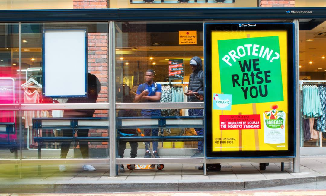 Adshel screen on bus stop, in front of retail shop with yellow and green food image