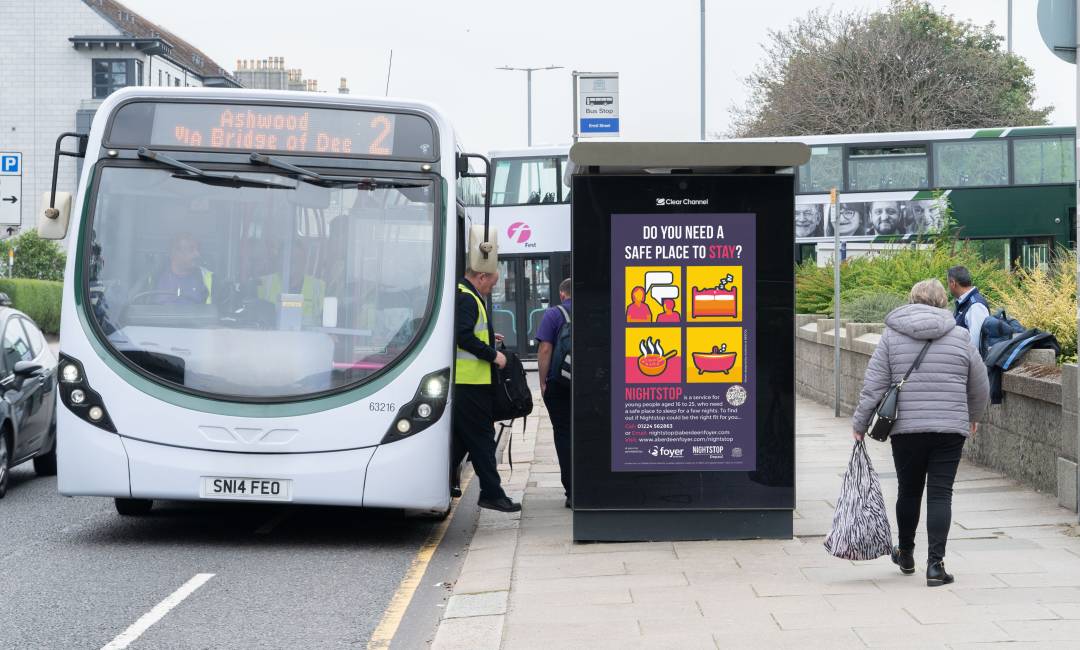 A Nightstop advert on display on the side of a Clear Channel UK bus shelter during the day as pedestrians walk by on the sidewalk