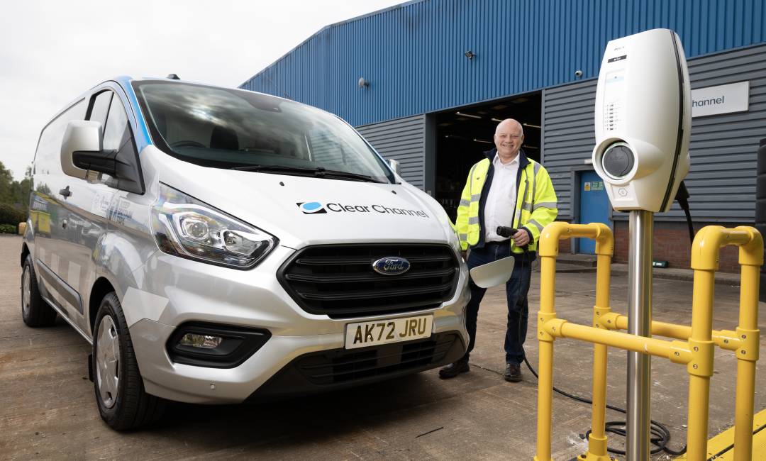 Clear Channel employee smiles as he plugs in a Ford Pro hybrid vehicle for charging