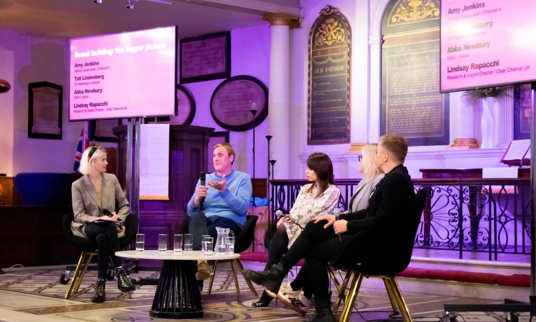 Five people sit on stage, male holds a microphone, in church setting