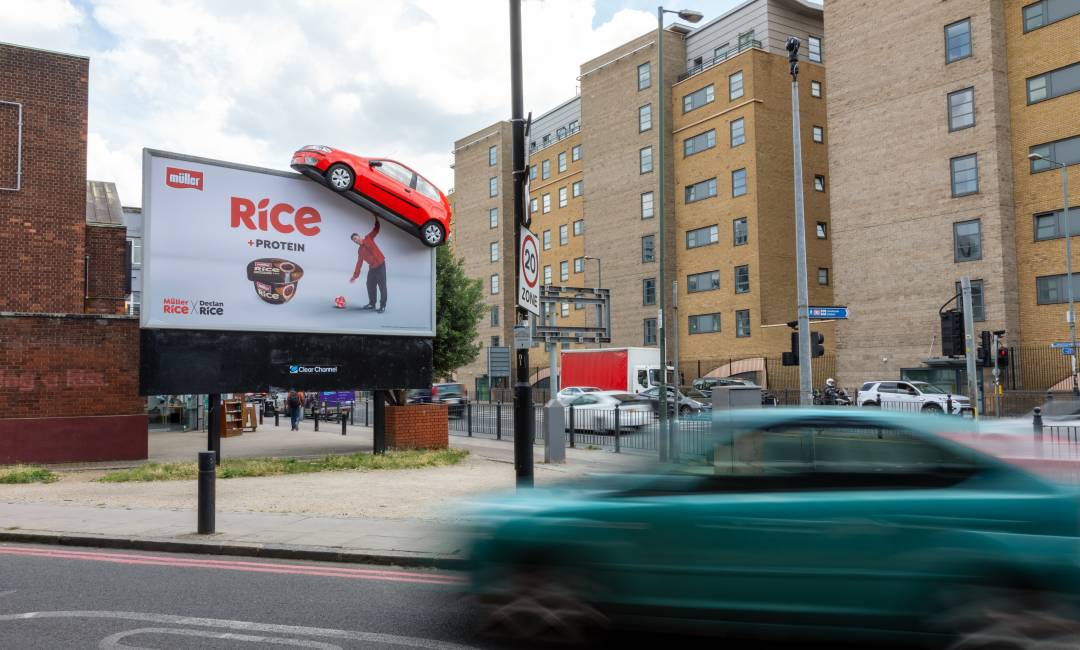 vehicles drive by a billboard showing Muller's campaign of footballer Declan Rice lifting a fake 3D car