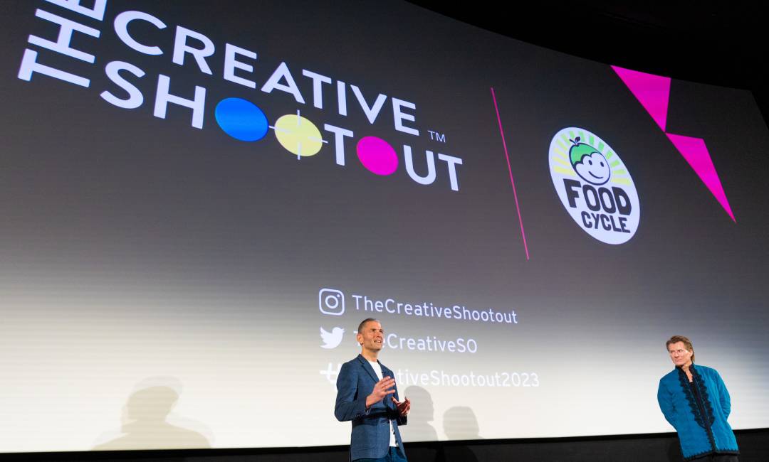 Two people presenting at The Creative Shootout 2023 in front of a large screen displaying The Creative Shootout logo