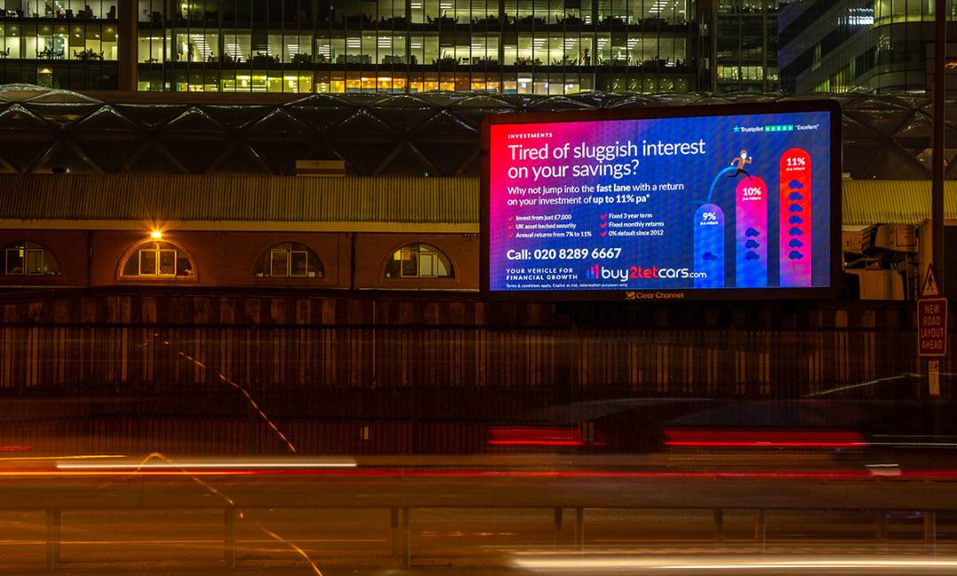 A roadside digital billboard at nighttime showing an ad for a car financing company