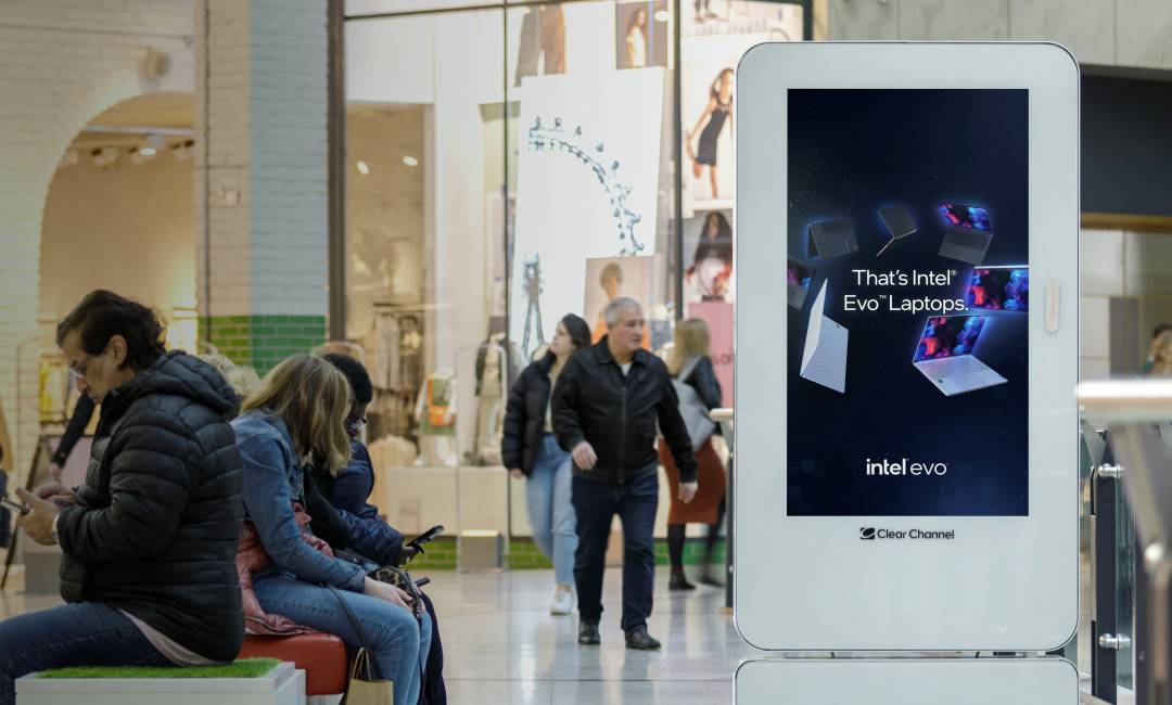 people sitting on phones in a shopping centre near a screen showing an Intel Evo advert