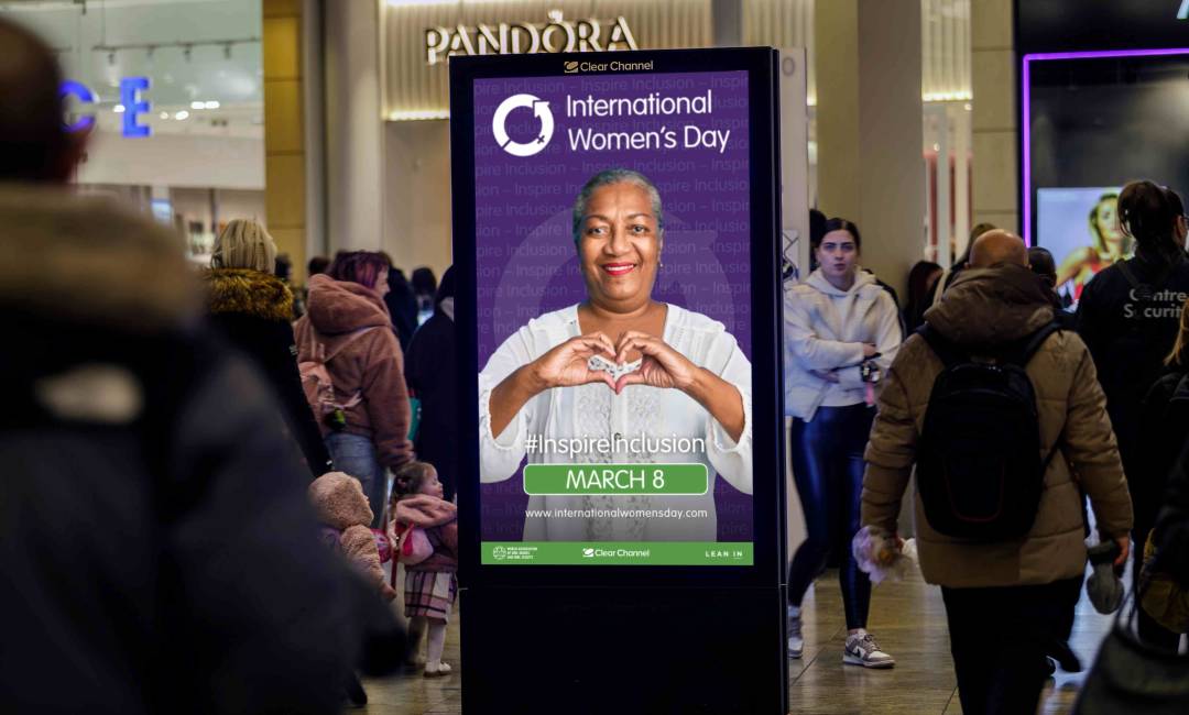 An international Women's Day advertisement displayed on a Malls Live screen in a busy shopping centre as pedestrians walk by