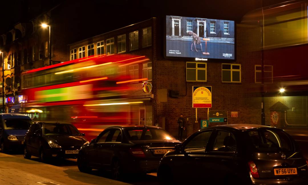 Digital billboard on the side of a building at nighttime as a bus drives by